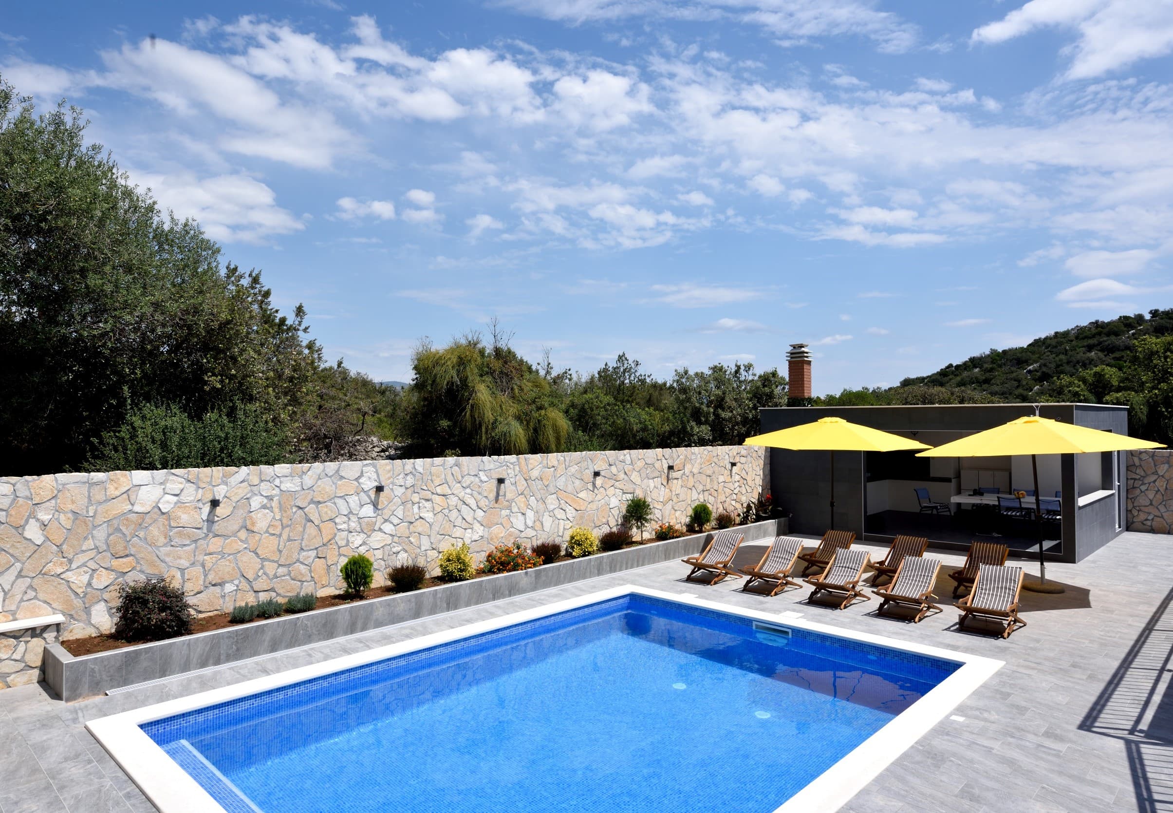 Heated pool in daytime with yellow umbrellas and loungers